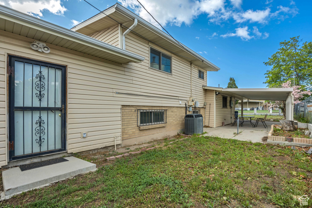 Back of property with central air condition unit, a patio area, and a lawn