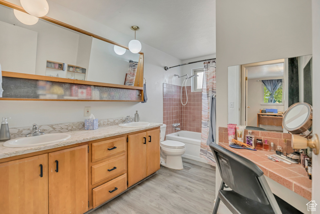 Full bath featuring double vanity, shower / tub combo with curtain, wood finished floors, toilet, and decorative backsplash