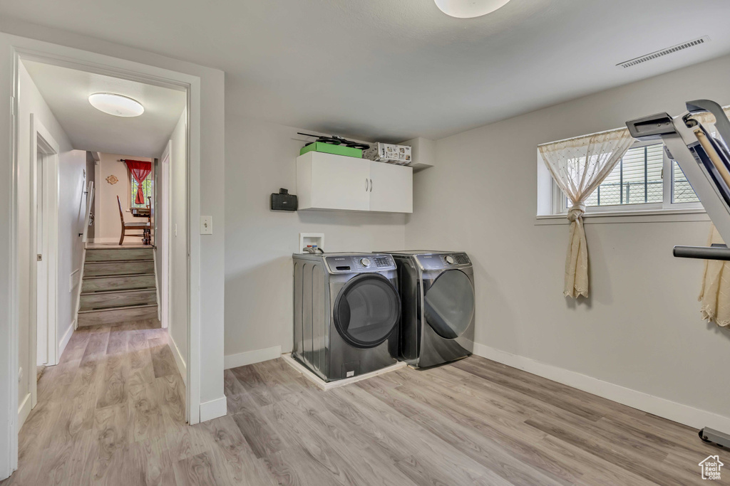 Laundry room with cabinet space, light wood-style flooring, separate washer and dryer, and baseboards