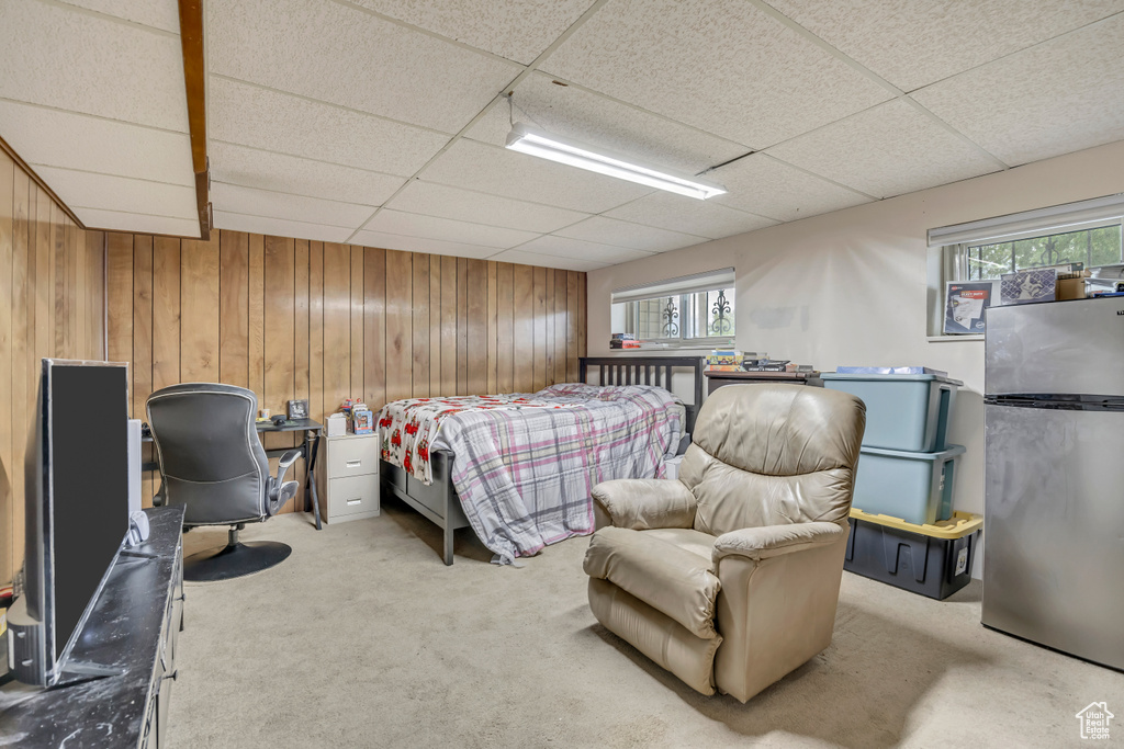 Bedroom with freestanding refrigerator, a paneled ceiling, carpet floors, wooden walls, and multiple windows