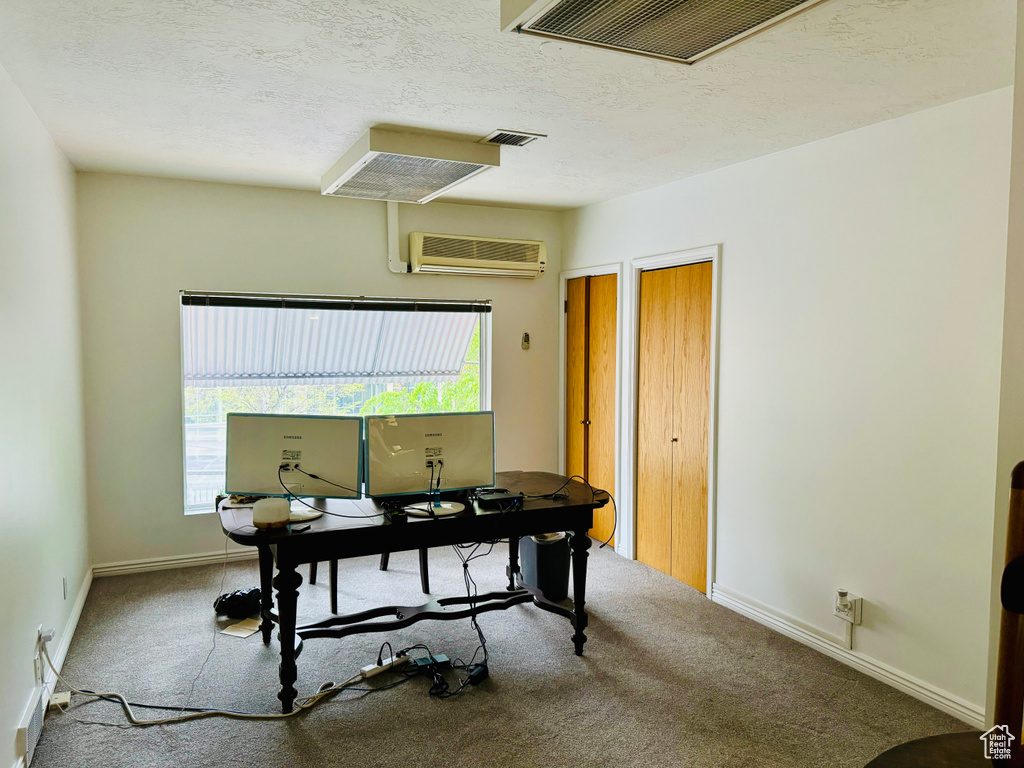 Carpeted office with a wall unit AC, baseboards, and a textured ceiling