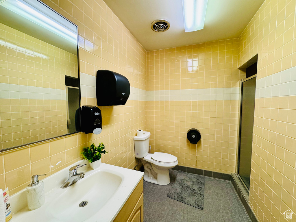 Bathroom featuring tile walls, a stall shower, toilet, vanity, and tile patterned floors