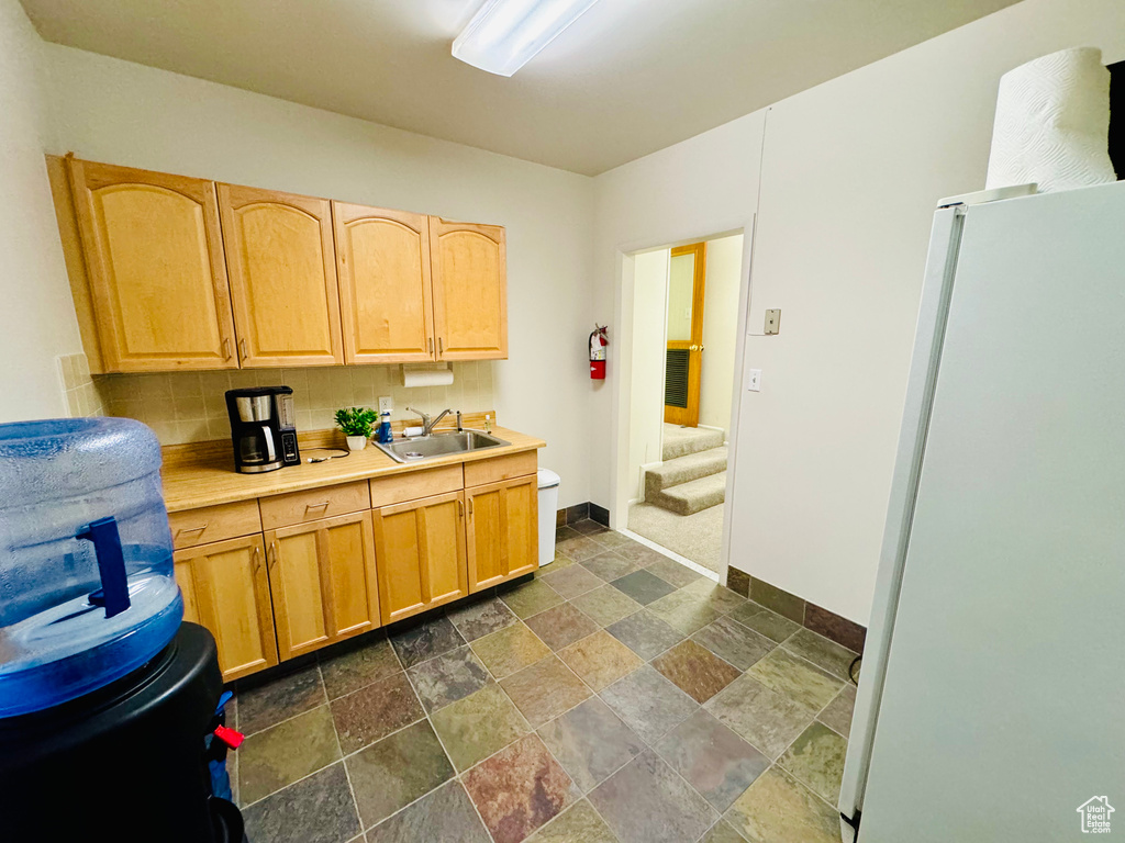 Kitchen with freestanding refrigerator, a sink, dark stone finish floors, baseboards, and light countertops