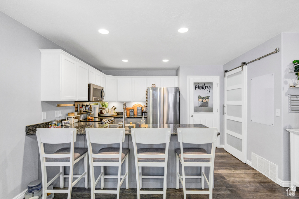 Kitchen featuring stainless steel appliances, a peninsula, recessed lighting, white cabinetry, and dark wood-style floors