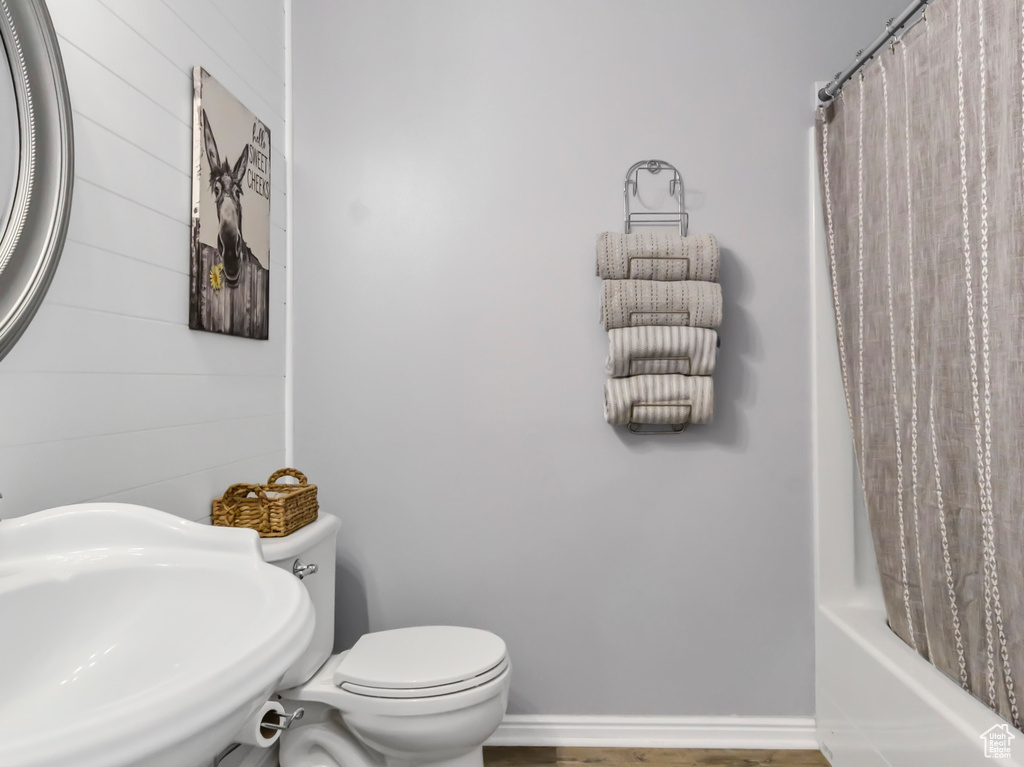 Full bathroom with wood finished floors, toilet, shower / tub combo, baseboards, and a textured ceiling
