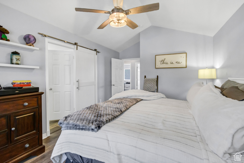 Bedroom featuring a barn door, vaulted ceiling, dark wood-type flooring, and a ceiling fan