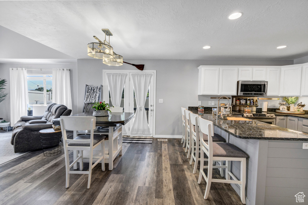 Kitchen featuring appliances with stainless steel finishes, dark stone counters, dark wood finished floors, white cabinetry, and recessed lighting