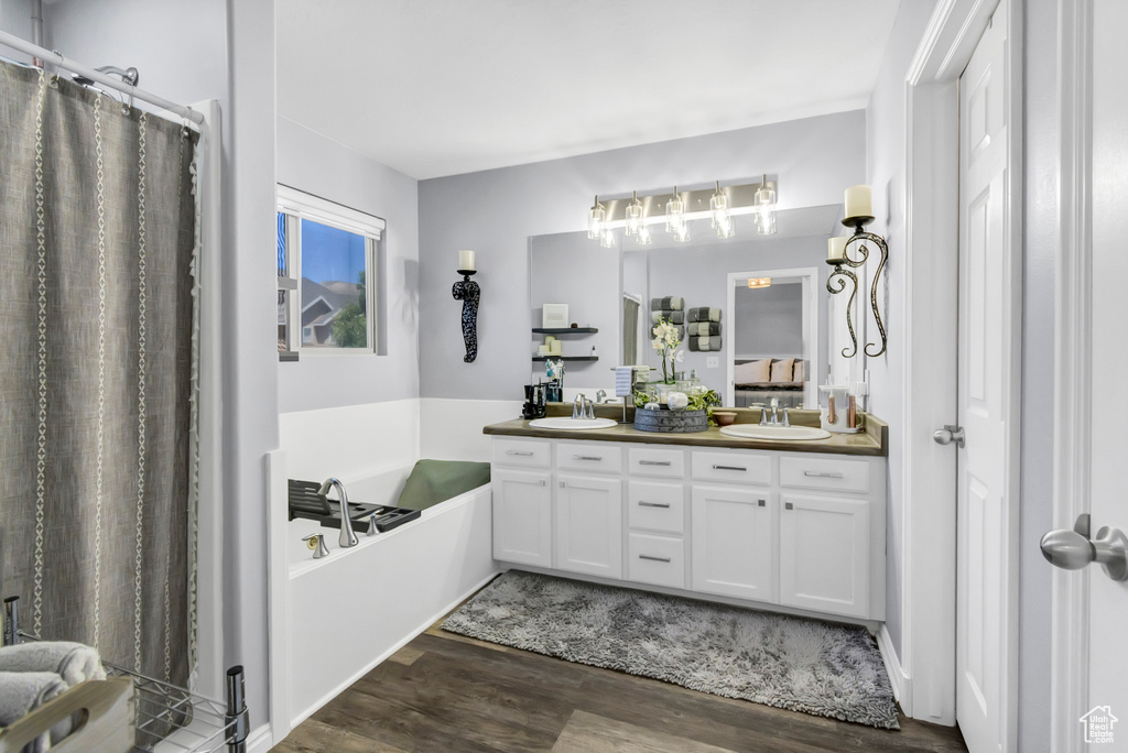 Bathroom with wood finished floors, double vanity, a garden tub, and a shower with curtain