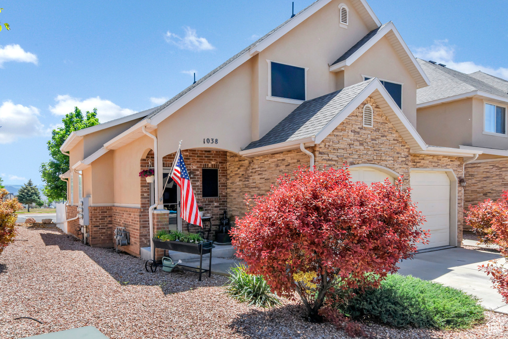 View of front of home with stucco siding, a garage, concrete driveway, and brick siding