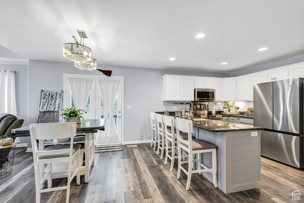 Kitchen with appliances with stainless steel finishes, a breakfast bar area, dark wood-type flooring, baseboards, and white cabinetry