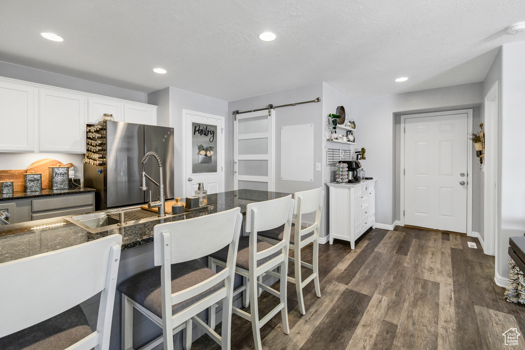 Kitchen featuring freestanding refrigerator, a barn door, a kitchen bar, white cabinets, and dark wood-type flooring