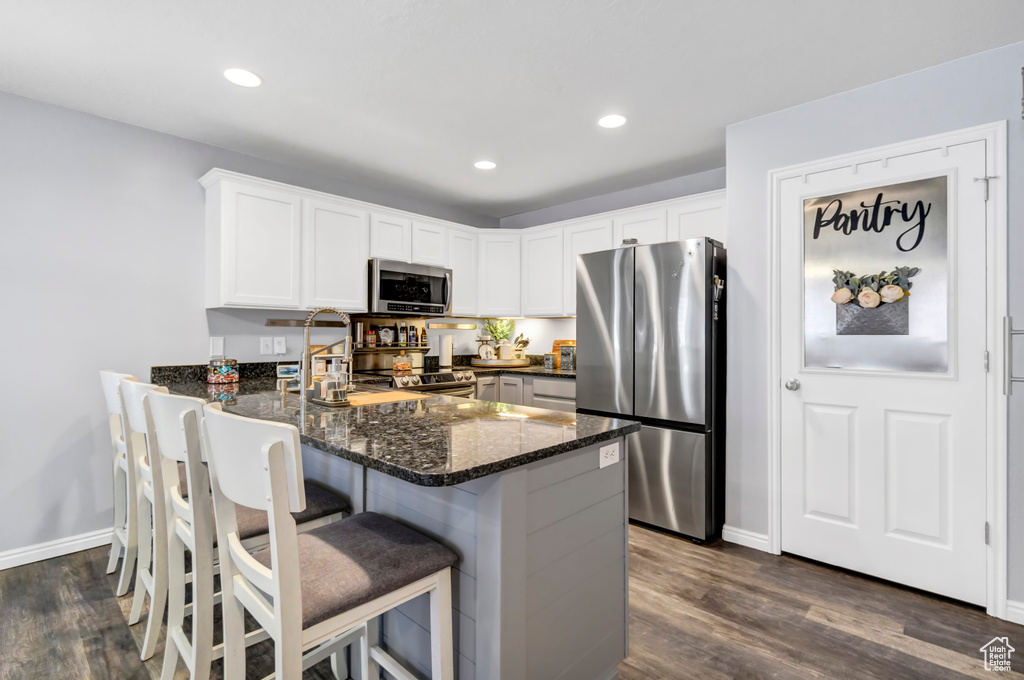 Kitchen featuring stainless steel appliances, dark stone countertops, a peninsula, dark wood-type flooring, and white cabinetry
