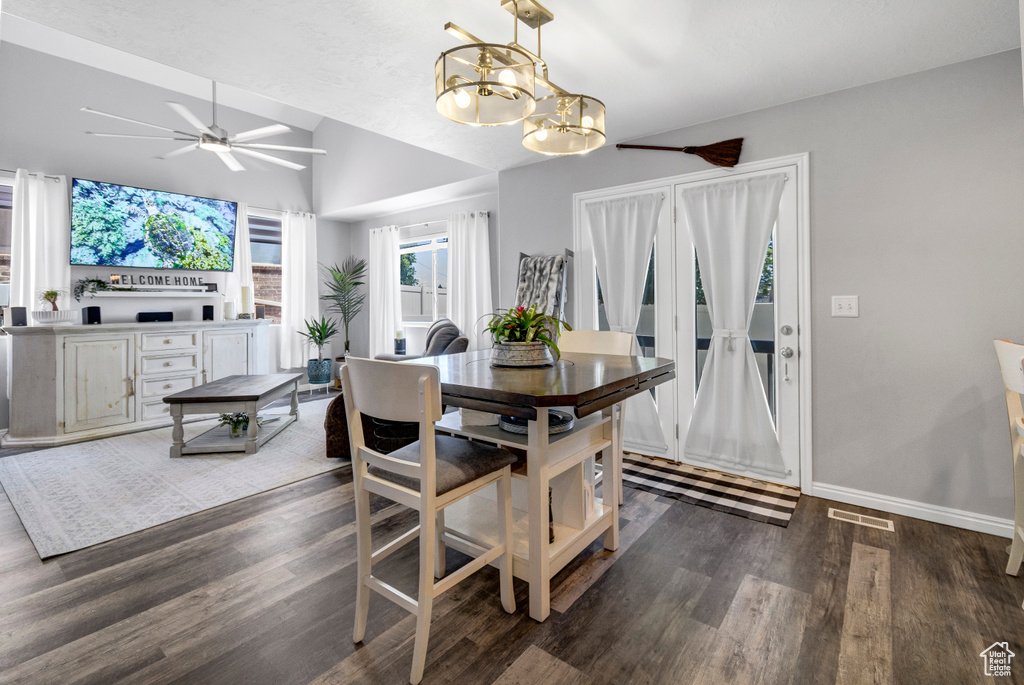 Dining room featuring vaulted ceiling, dark wood-style flooring, a chandelier, ceiling fan, and baseboards