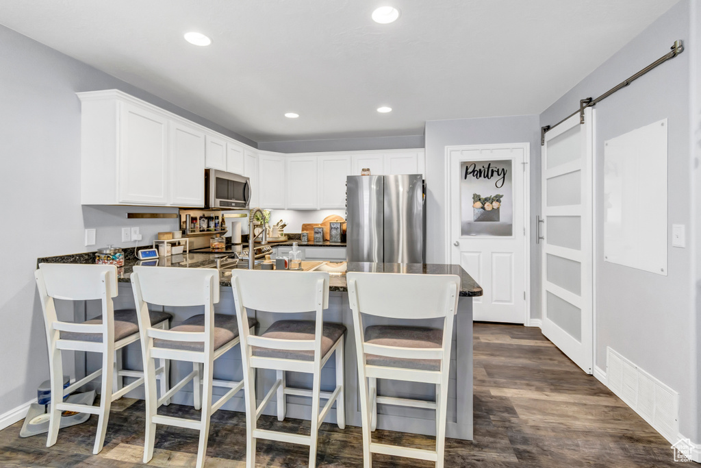 Kitchen with appliances with stainless steel finishes, a peninsula, dark countertops, white cabinetry, and dark wood finished floors