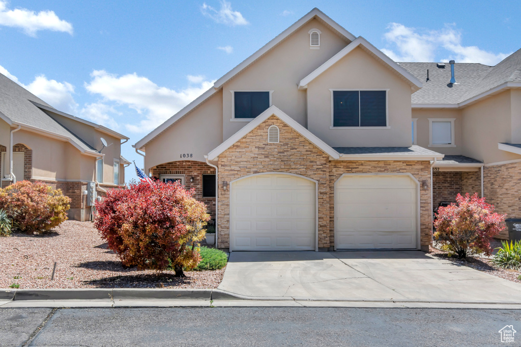 View of front of home with stucco siding, driveway, a garage, and stone siding