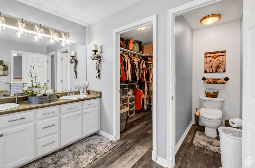 Full bathroom featuring wood finished floors, double vanity, toilet, a walk in closet, and baseboards