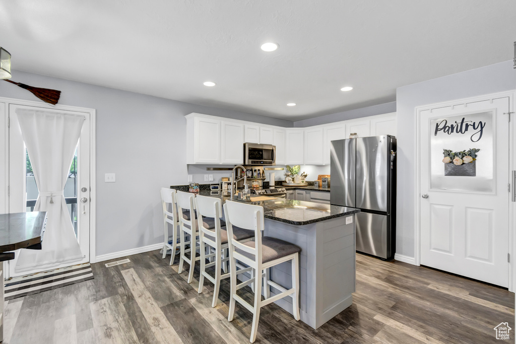 Kitchen featuring appliances with stainless steel finishes, dark wood-style floors, dark stone countertops, white cabinets, and baseboards
