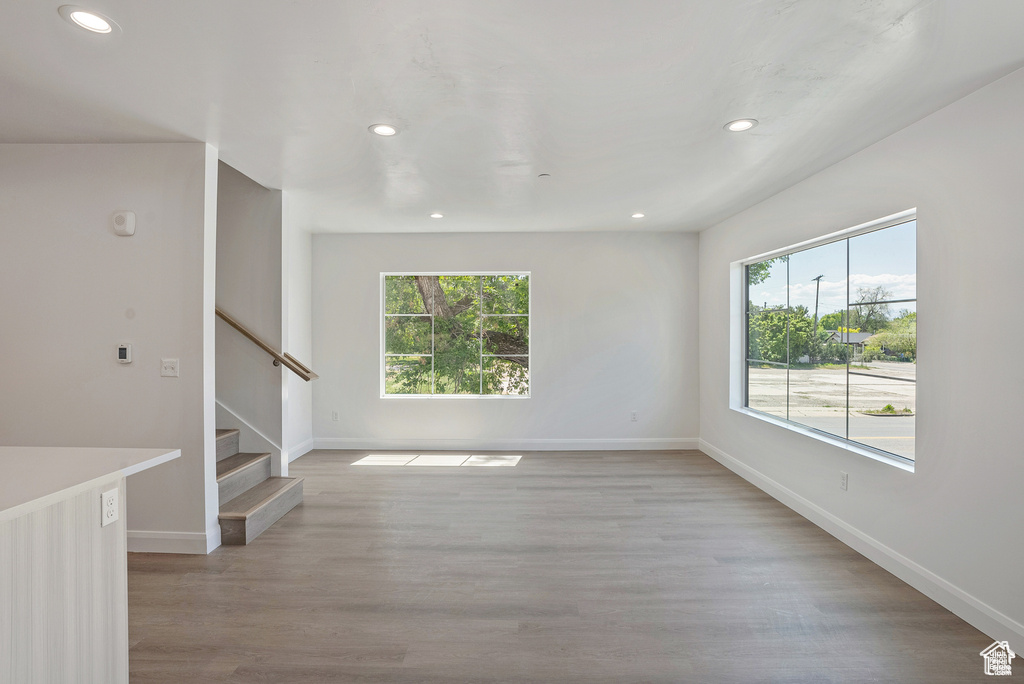 Unfurnished room featuring healthy amount of natural light, recessed lighting, stairs, baseboards, and light wood-style floors