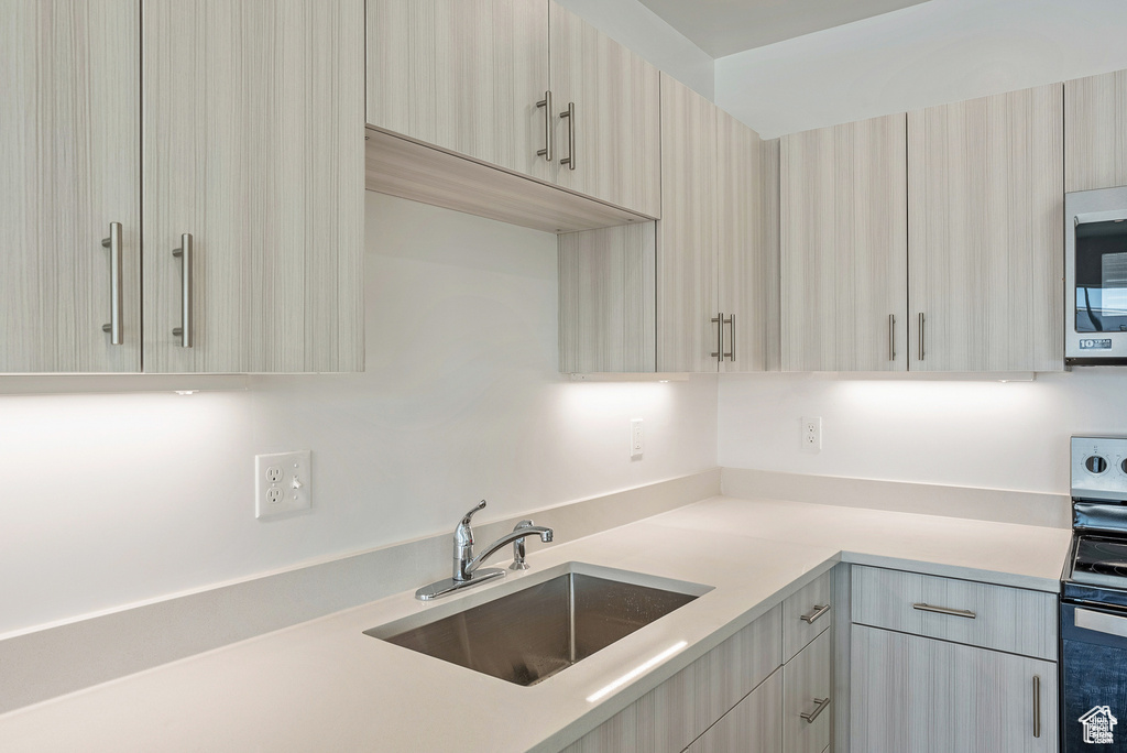 Kitchen featuring modern cabinets, appliances with stainless steel finishes, light countertops, and a sink