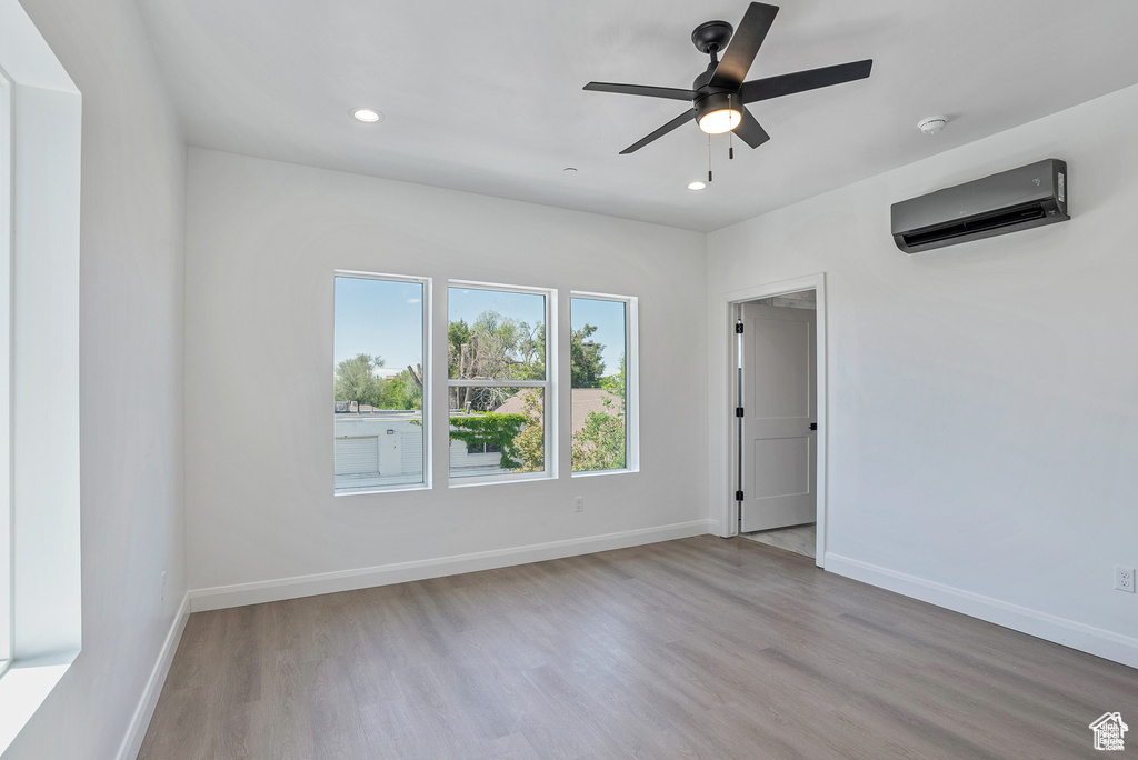 Empty room featuring an AC wall unit, wood finished floors, baseboards, recessed lighting, and a ceiling fan