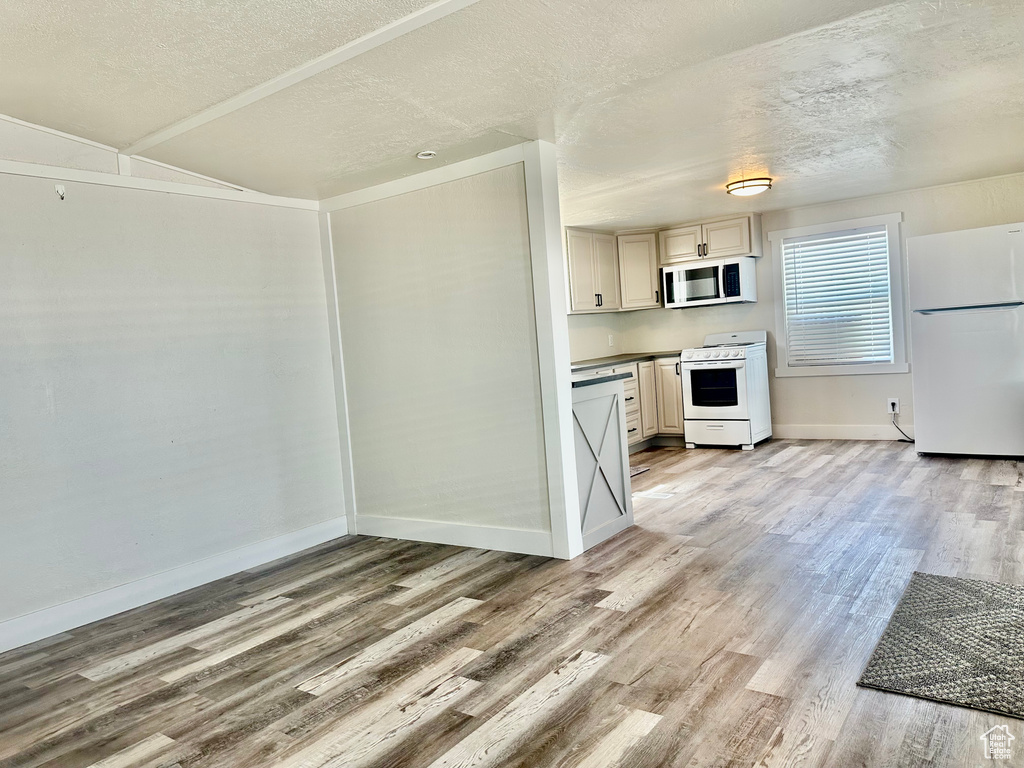 Kitchen featuring white appliances, light wood finished floors, a textured ceiling, baseboards, and vaulted ceiling