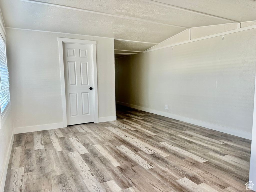 Empty room with wood finished floors, baseboards, vaulted ceiling, and a textured ceiling
