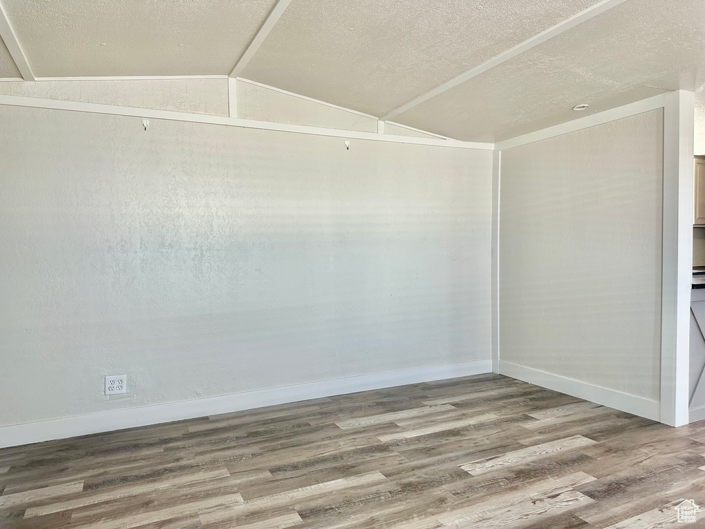 Spare room featuring vaulted ceiling, wood finished floors, a textured ceiling, and baseboards