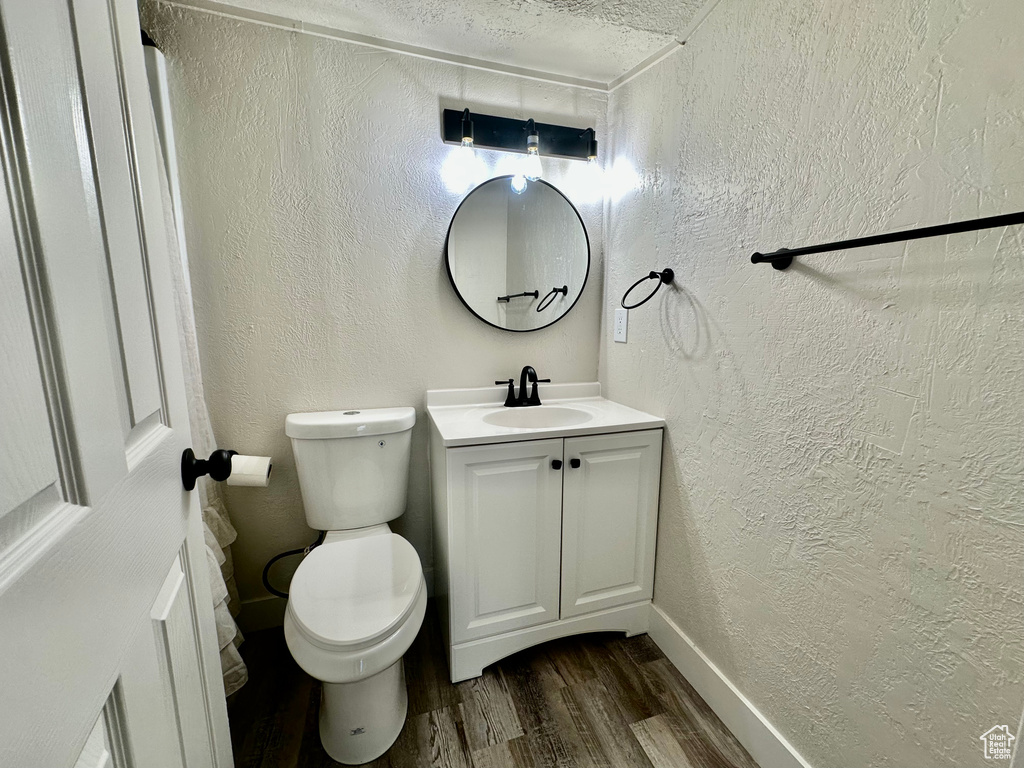 Bathroom featuring wood finished floors, vanity, a textured wall, toilet, and baseboards