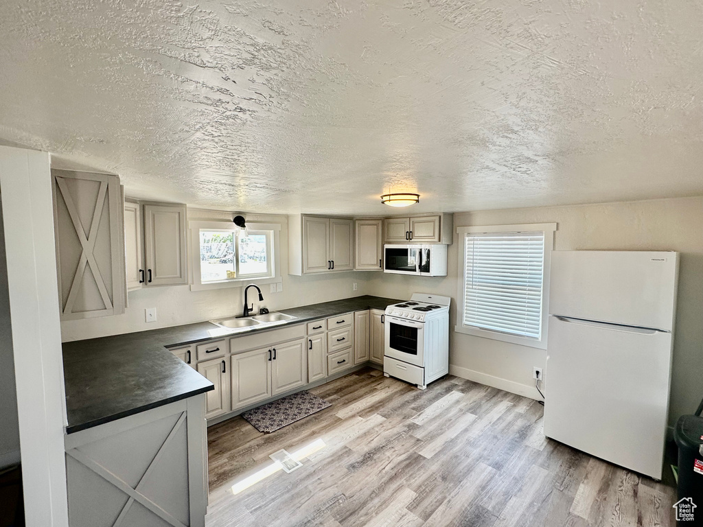 Kitchen featuring white appliances, dark countertops, a sink, light wood-type flooring, and a textured ceiling