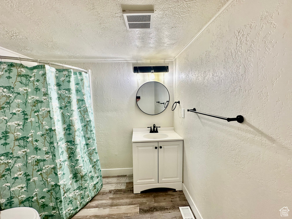 Full bathroom featuring a textured wall, a textured ceiling, vanity, wood finished floors, and a shower with shower curtain
