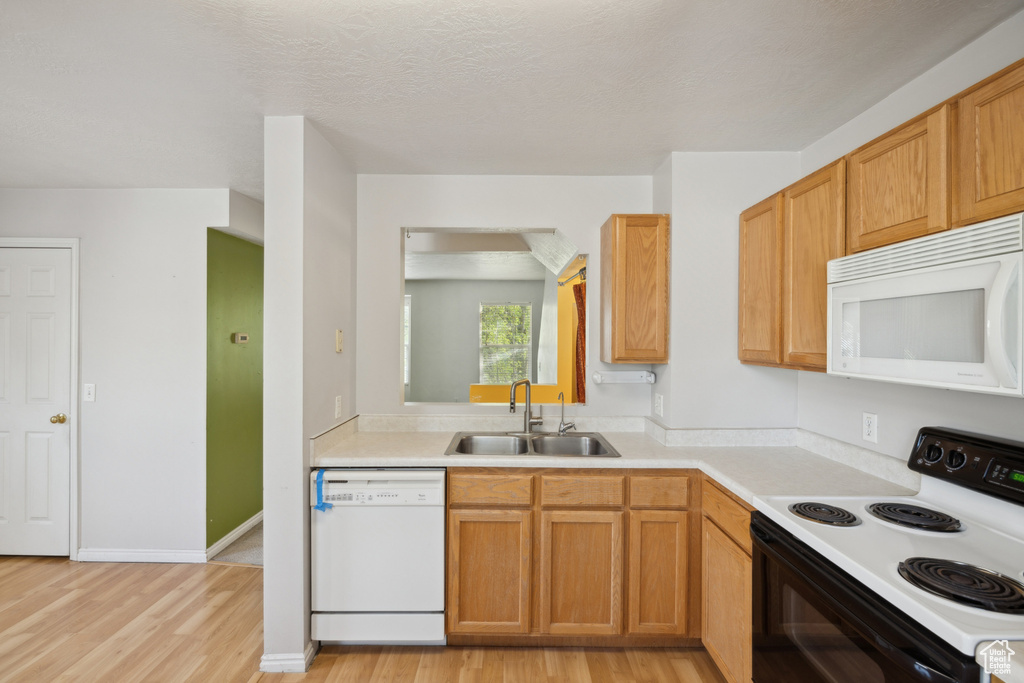 Kitchen with white appliances, a sink, light wood-type flooring, and light countertops