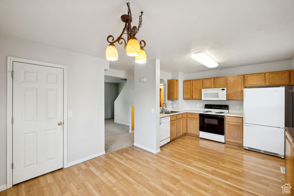 Kitchen with white appliances, light countertops, light wood finished floors, baseboards, and pendant lighting