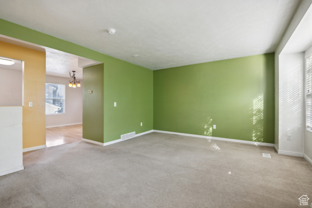 Carpeted empty room featuring a chandelier, baseboards, and a smoke detector