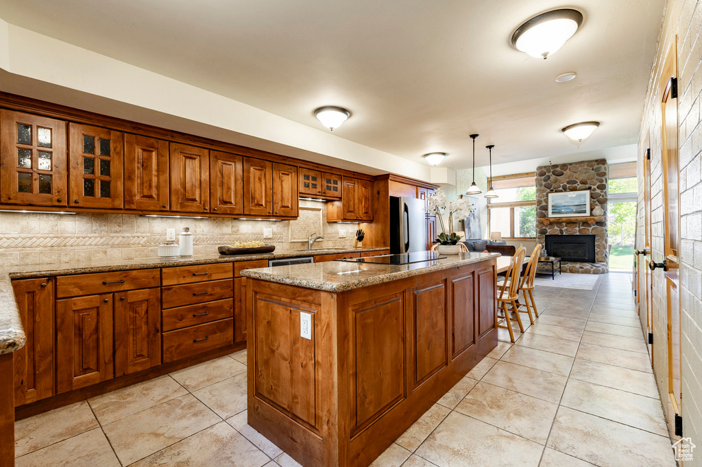Kitchen with brown cabinetry, a sink, a center island, backsplash, and light stone counters