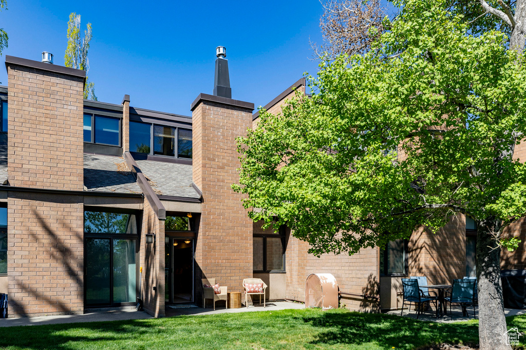 Back of property with a chimney, a lawn, and brick siding