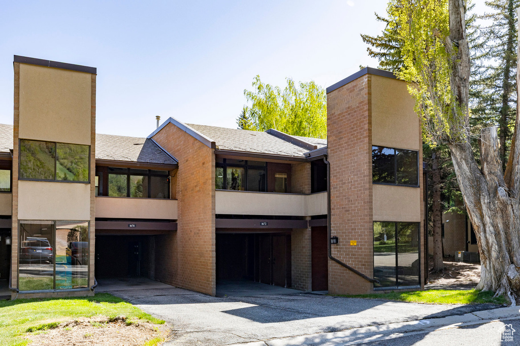 View of front of home featuring stucco siding, brick siding, a chimney, and a shingled roof