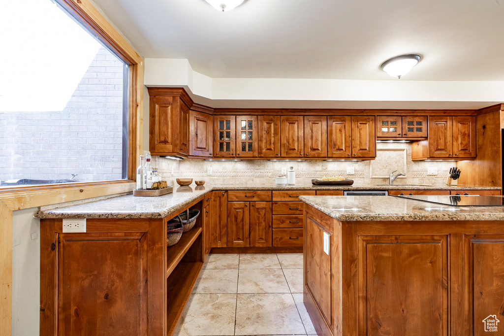 Kitchen featuring brown cabinetry, decorative backsplash, and light stone counters