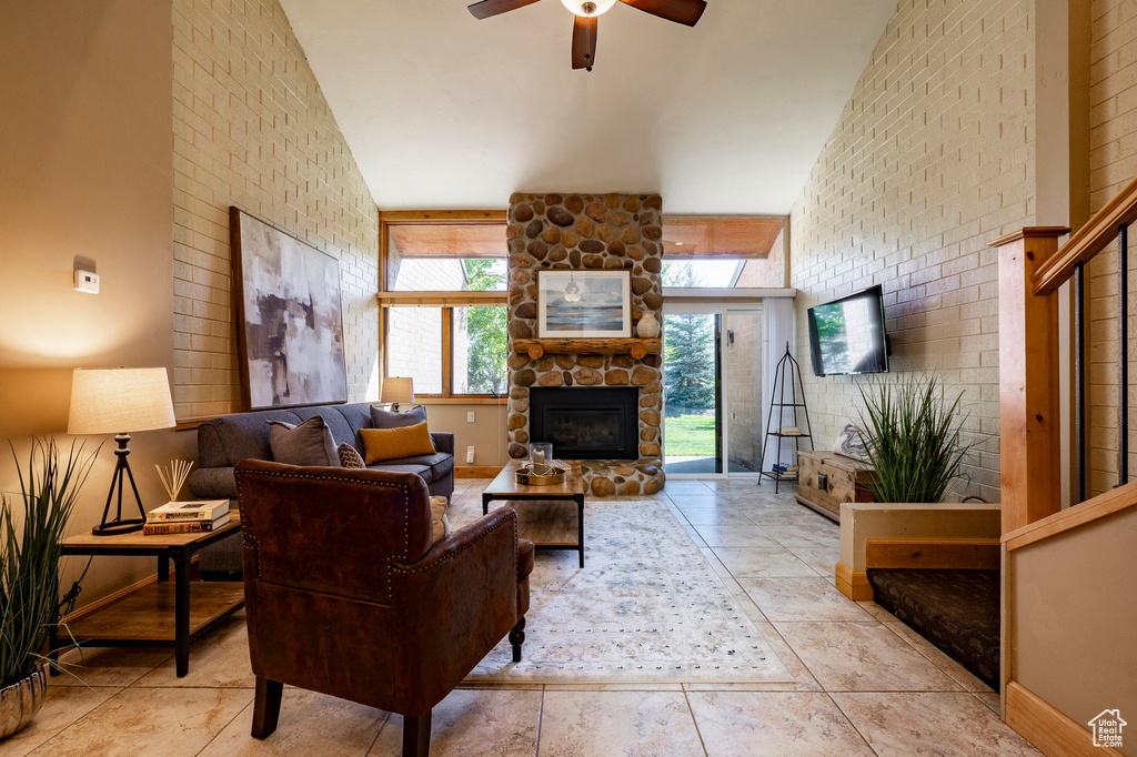 Living room with a ceiling fan, a stone fireplace, and baseboards