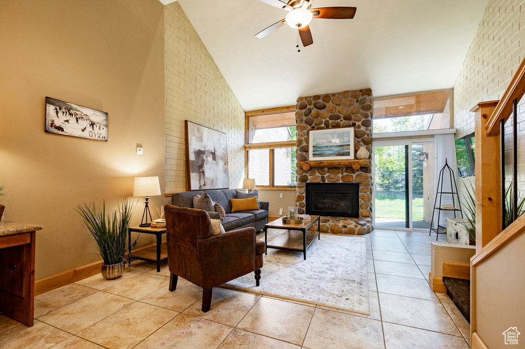 Living room with high vaulted ceiling, a ceiling fan, a stone fireplace, light tile patterned flooring, and healthy amount of natural light
