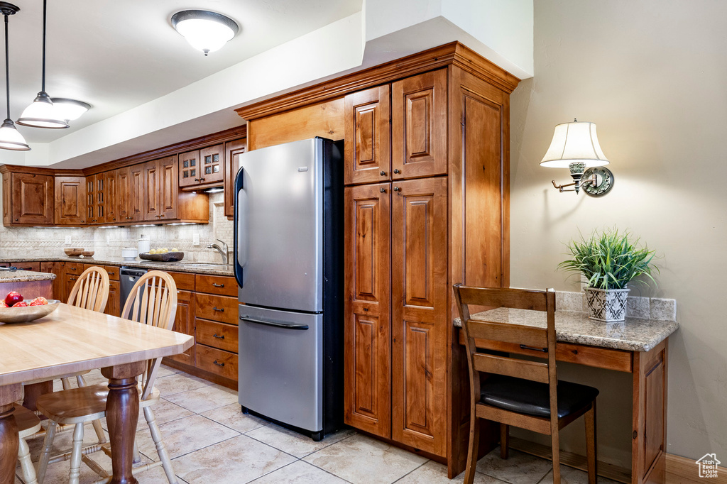 Kitchen featuring freestanding refrigerator, brown cabinets, tasteful backsplash, and light stone counters