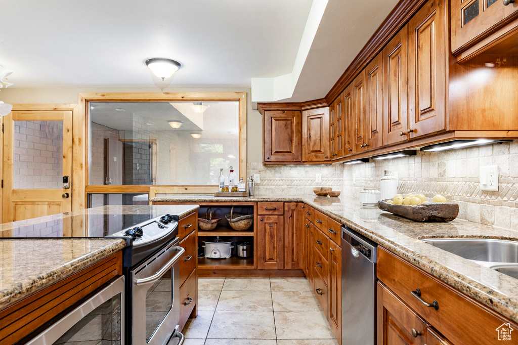 Kitchen featuring appliances with stainless steel finishes, brown cabinets, light stone counters, and backsplash