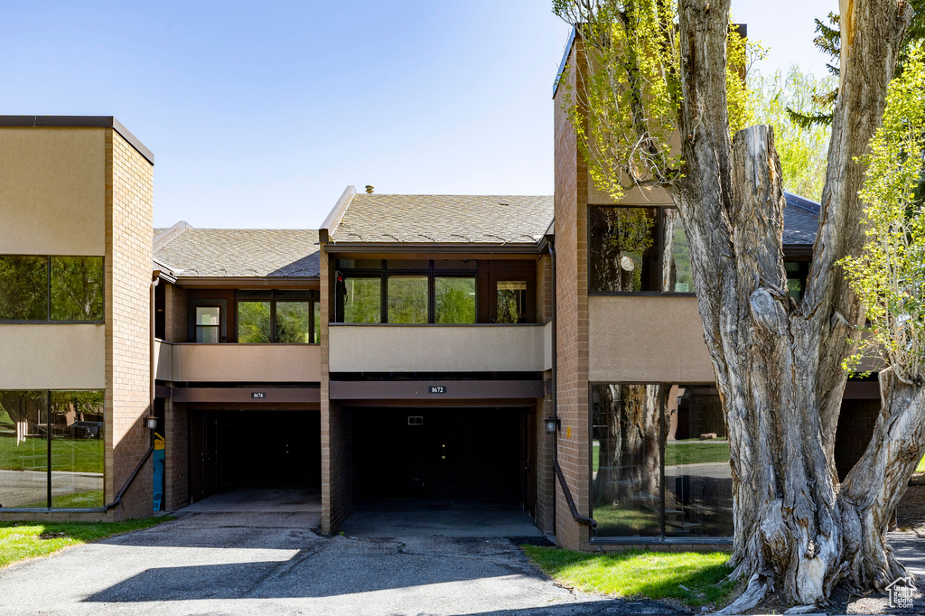 View of front of property with roof with shingles, stucco siding, driveway, and a garage