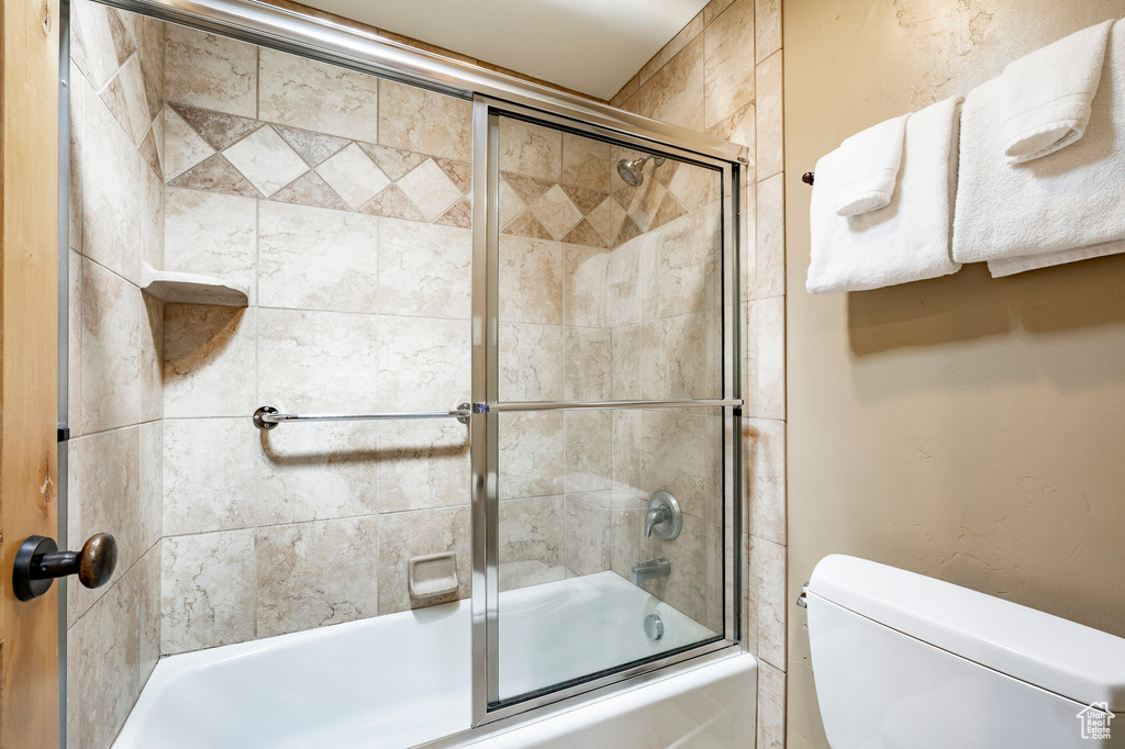 Full bath featuring bath / shower combo with glass door and toilet