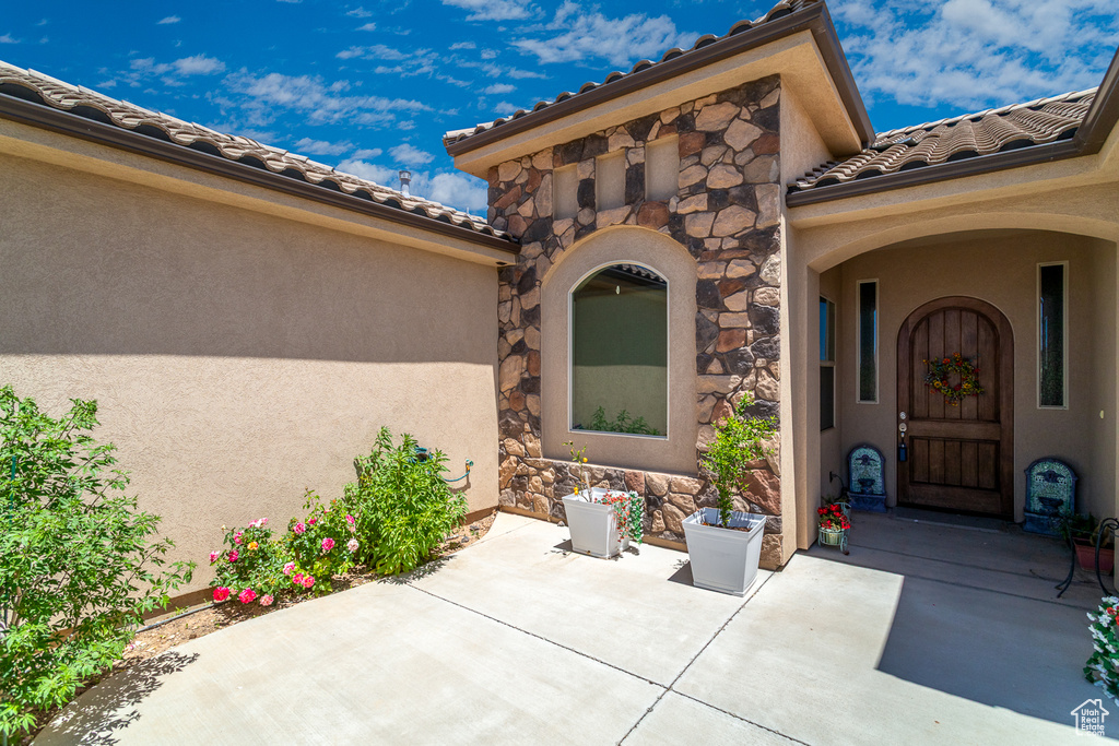 Property entrance featuring stone siding, a patio, stucco siding, and a tiled roof
