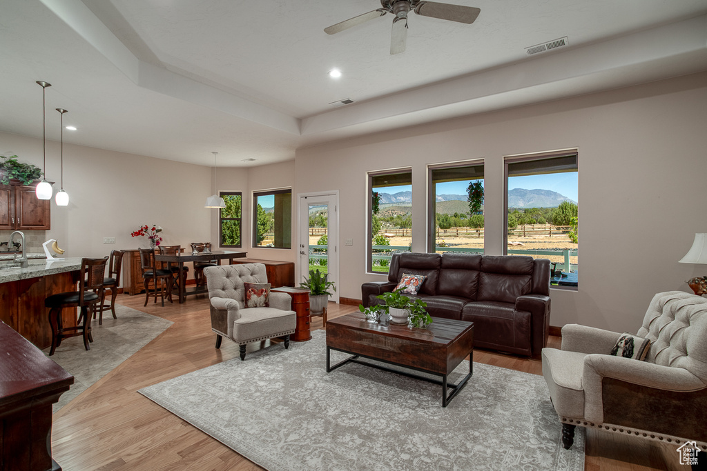 Living room with a raised ceiling, recessed lighting, light wood finished floors, and ceiling fan