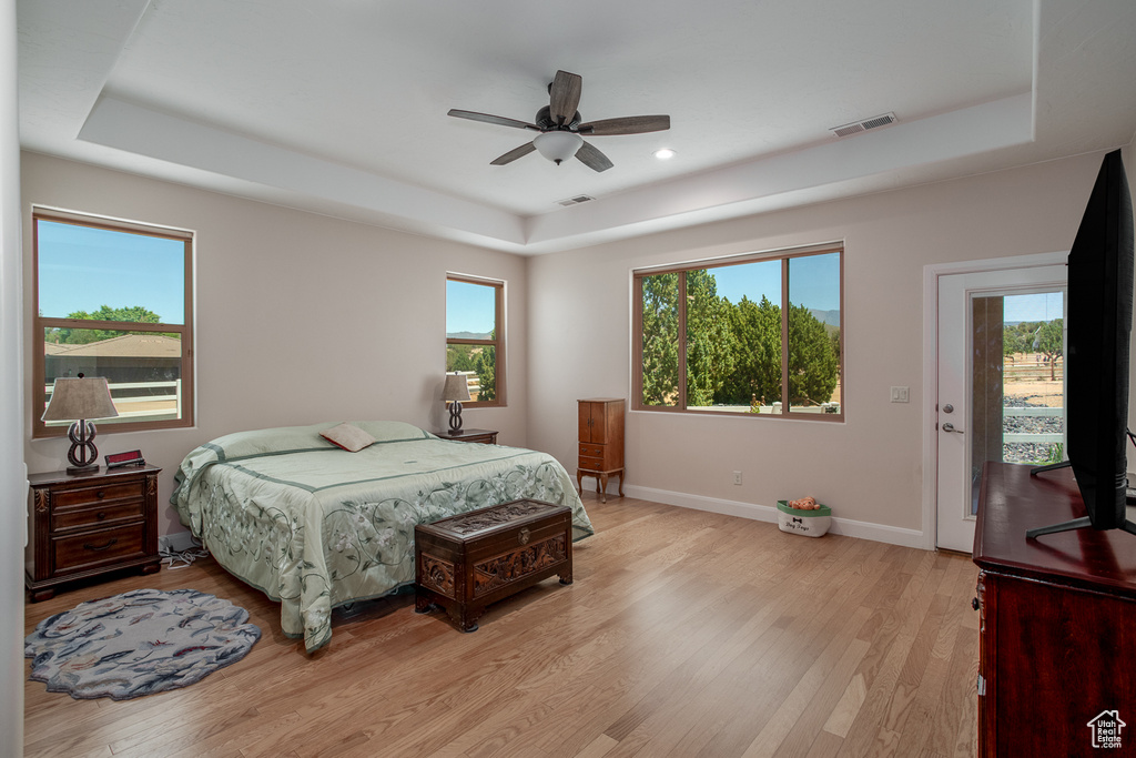 Bedroom with a tray ceiling, light wood-type flooring, multiple windows, and recessed lighting