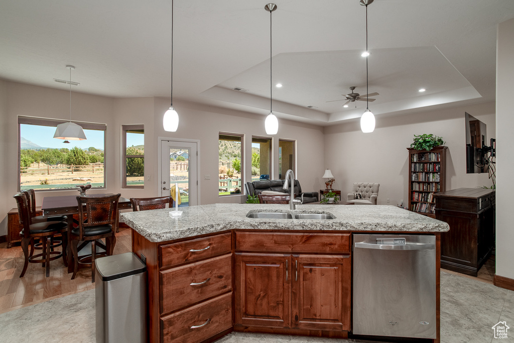 Kitchen featuring stainless steel dishwasher, a sink, a raised ceiling, open floor plan, and decorative light fixtures