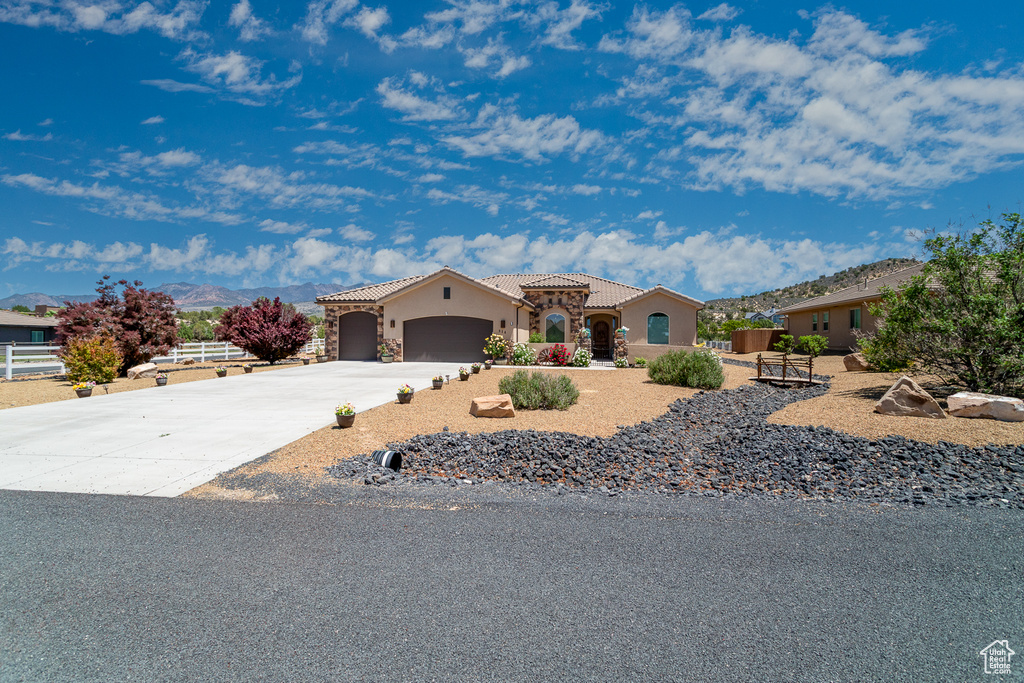 Mediterranean / spanish house with stucco siding, a garage, a tile roof, driveway, and a mountain view