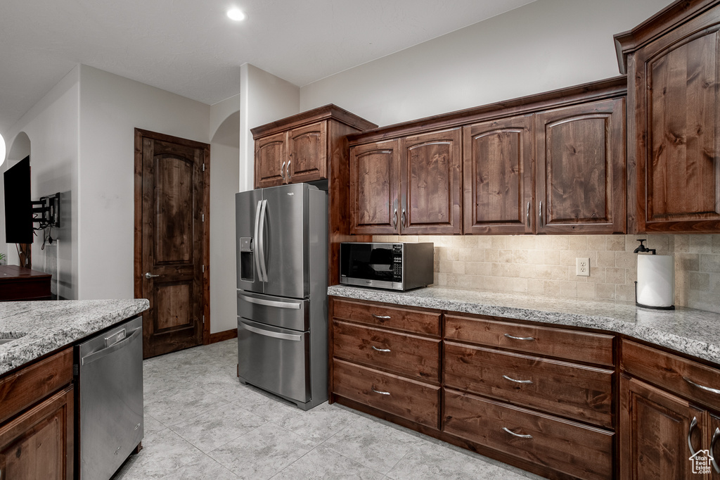Kitchen with stainless steel appliances, arched walkways, light stone counters, and tasteful backsplash