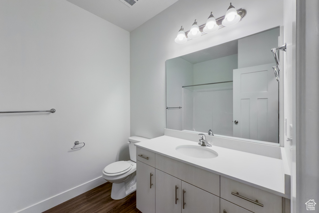 Bathroom featuring vanity, wood finished floors, baseboards, toilet, and a shower